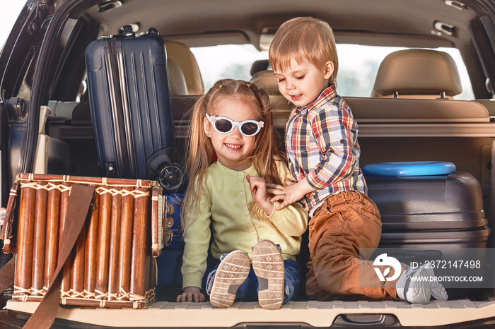 旅行开始了。小可爱的孩子们拿着行李箱在汽车后备箱里玩耍。家庭公路tr