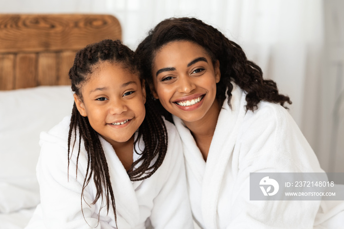 Home Portrait Of Happy African American Mom And Daughter In White Bathrobes