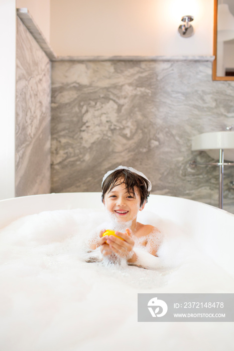 Portrait of boy (6-7) sitting in bathtub with soap in hand