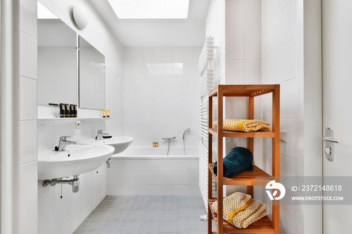 Shelves with towels and drying rack located near sinks with mirrors and bathtub in light bathroom of