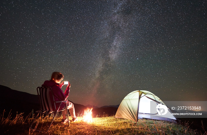 Female hiker having a rest at summer night camping in the mountains beside campfire and glowing tour