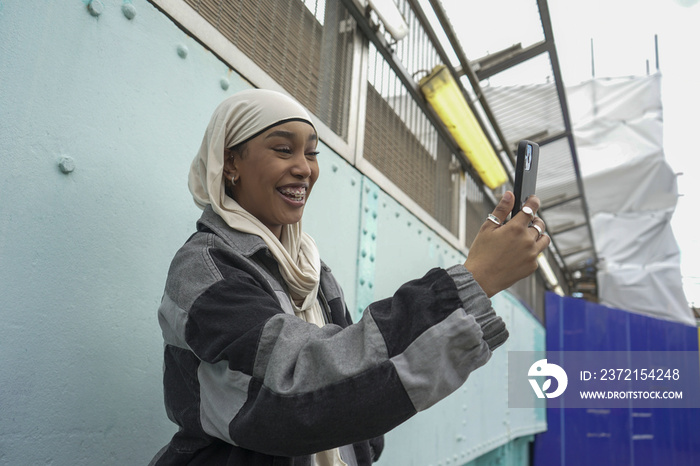 Smiling young woman wearing hijab taking selfie in city