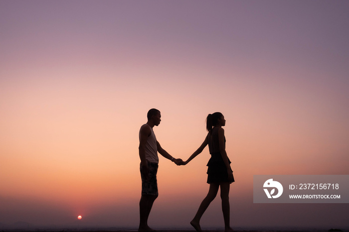 silhouette of couple holding hand and walk at sunset