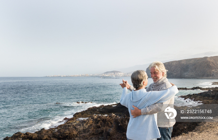 Happy couple of senior people dancing and smiling on the cliff. Two persons with gray hair, casual c