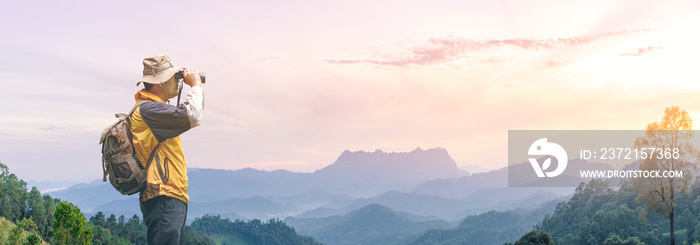 背包徒步旅行者拿着双筒望远镜在岩石山顶上眺望。全景