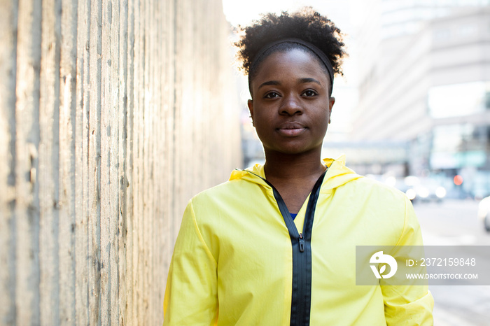 Portrait of serious female athlete standing on sidewalk by wall in city