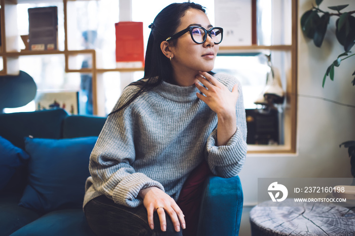 Thoughtful casual hipster girl in casual wear recreating at cozy interior pondering on idea during l