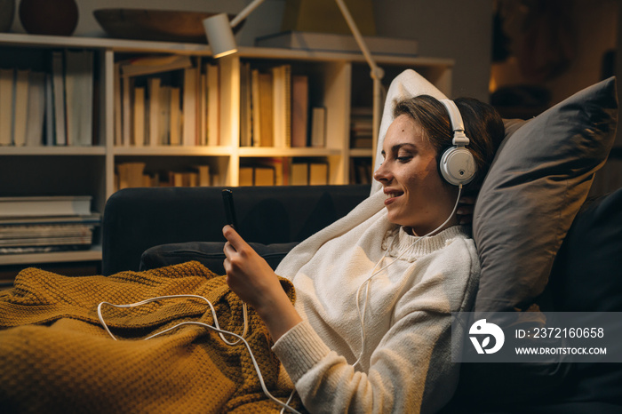 woman laying on sofa and listening to a music on headphones