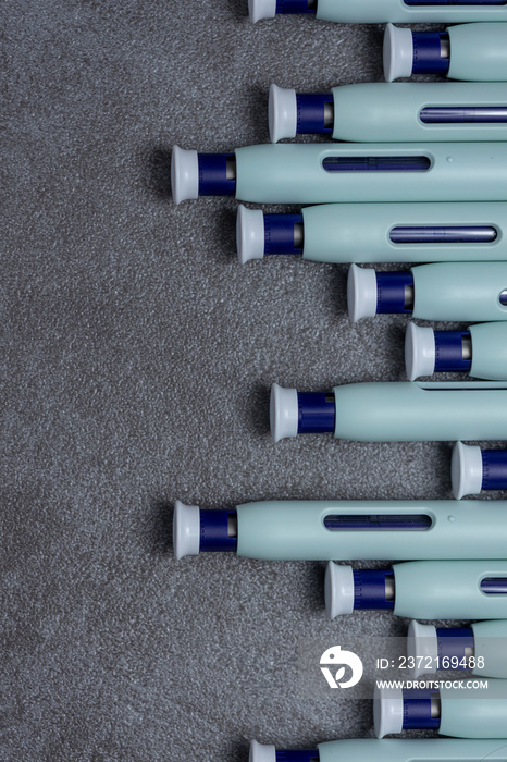 Layout graphic of a row of syringe self application pens against a rustic textured gray background. 