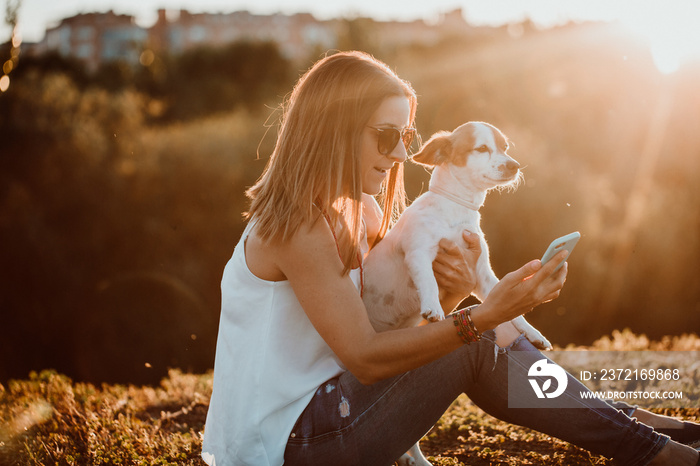 .Pretty young woman taking pictures with her sweet little dog with her smartphone on a sunny summer 