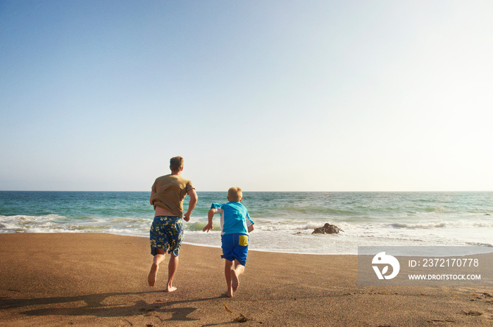 Rear view of father and son running at beach against clear sky