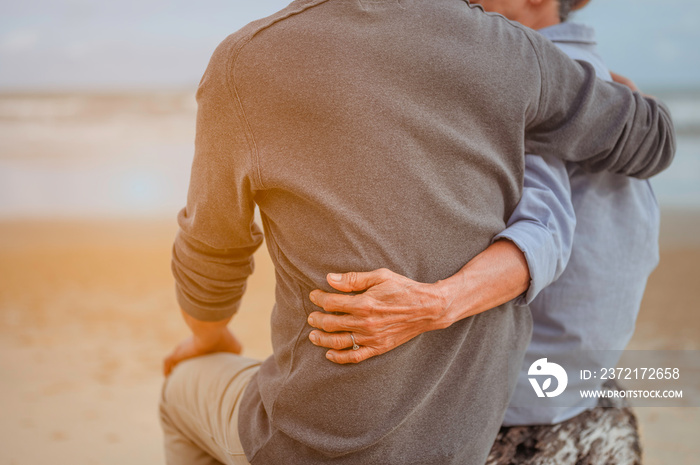 Retirement couple  on a summer evening watch sea, Woman hugging her husband at the beach at sunset.