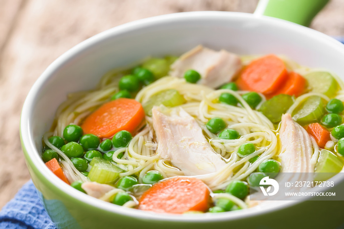 Fresh homemade chicken noodle soup with carrot, peas and celery in green soup bowl (Selective Focus,