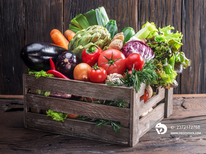 Fresh multi-colored vegetables in wooden crate. Wooden background.