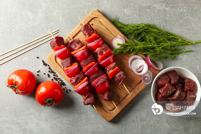 Board with raw shish kebab and ingredients on gray background