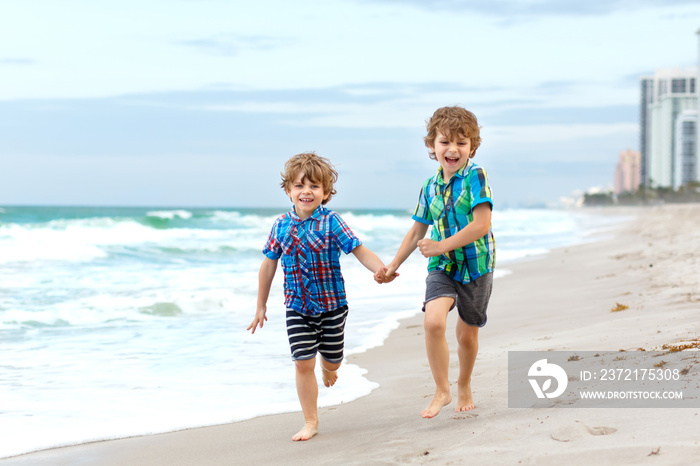 Two little kids boys running on the beach of ocean