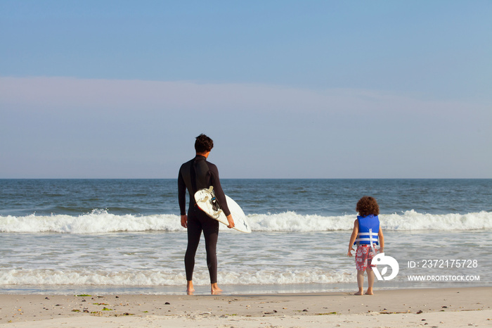 Surfer standing with son (2-3) on beach