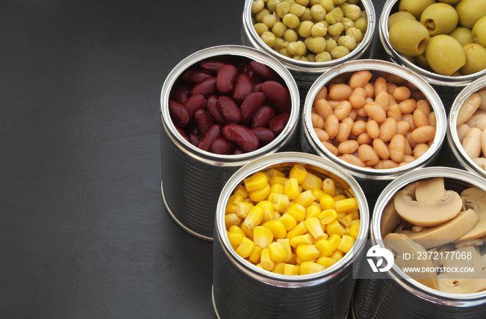 Canned green peas, beans, corn, olives and mushrooms on black table.