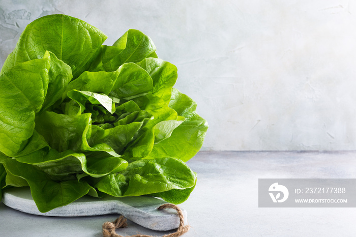 Head of fresh organic lettuce salad on marble cutting board on light gray stone background. Healthy 