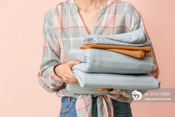 Woman holding stack of clean bed sheets on color background