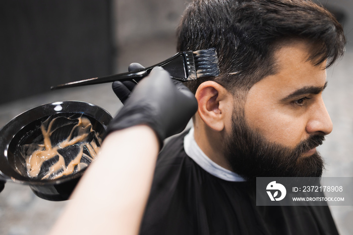 Professional barber dying male client hair in barbershop. Hairdresser applies dye to the clients ha