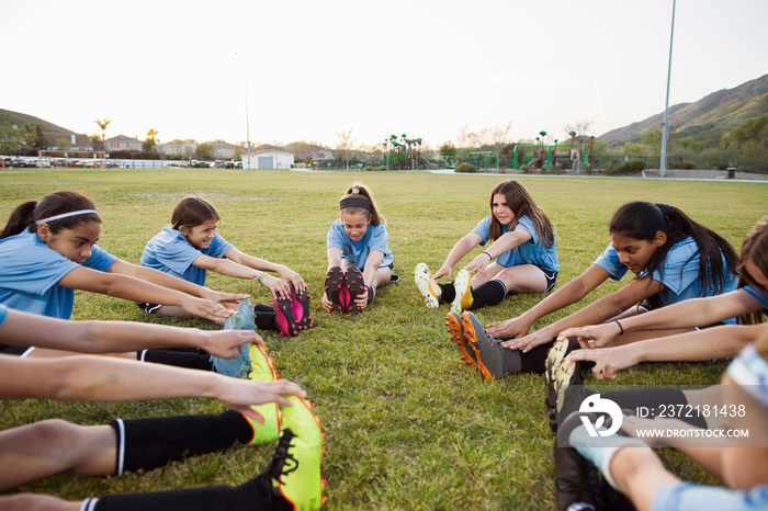 Girls exercising while sitting on soccer field against clear sky during sunset