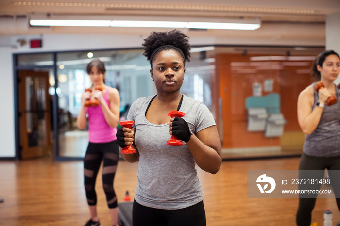 Confident female athletes looking away while exercising with dumbbells in gym