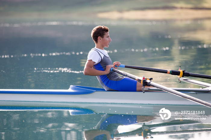 A Young single scull rowing competitor paddles on the tranquil lake