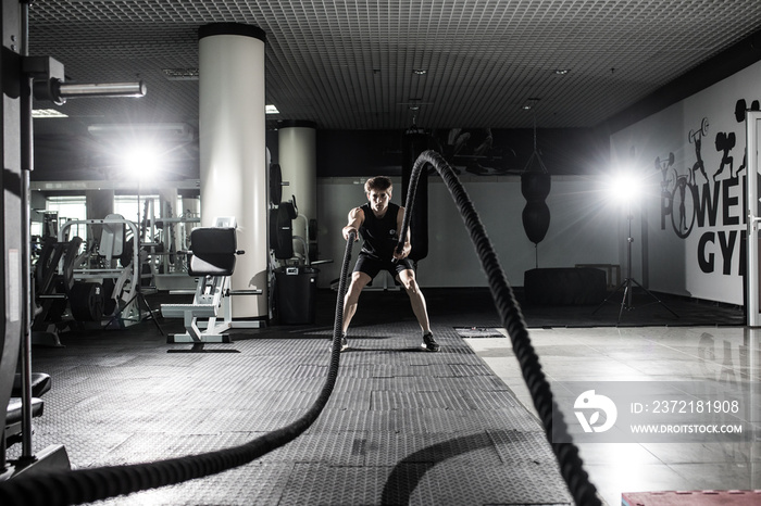 Strong Men with battle rope battle ropes exercise in the fitness gym. CrossFit.