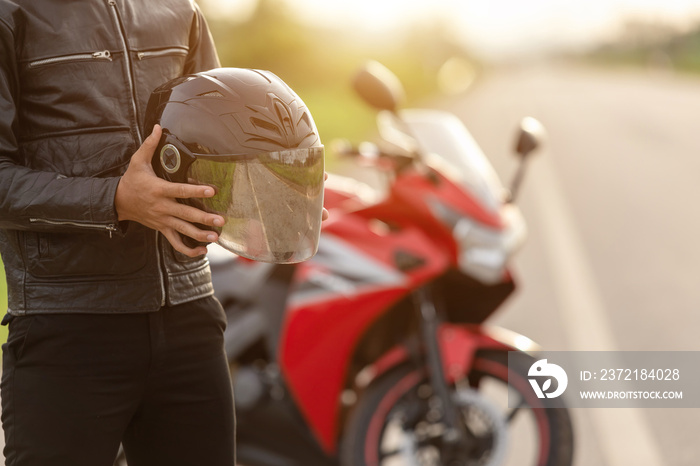 Handsome motorcyclist wear leather jacket and holding helmet on the road