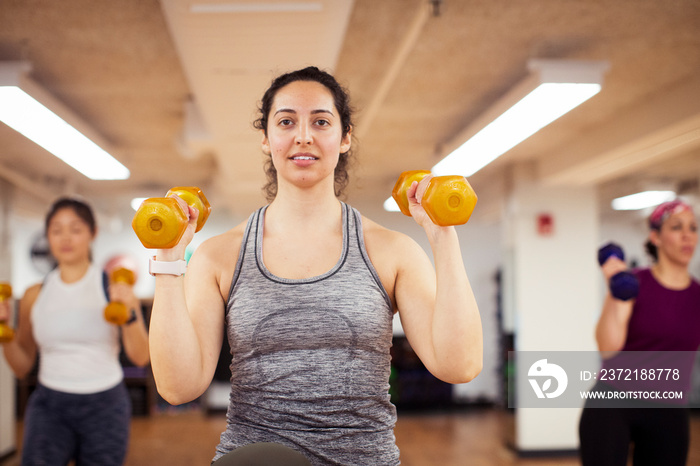 Confident female athletes lifting dumbbells while standing in gym