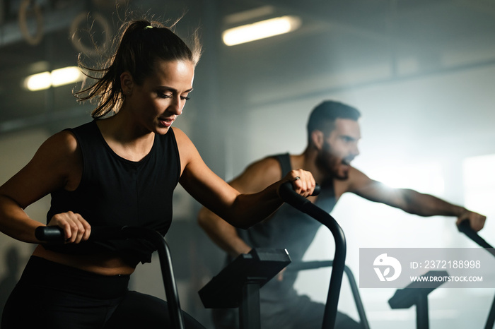 Young athletes cycling on exercise bikes while working out in a gym.