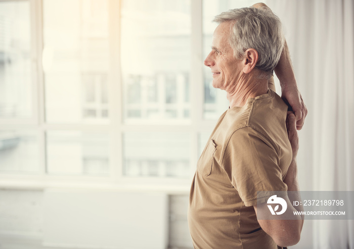 Side view profile of cheerful mature man with hands hooked behind his back. Copy space in left side