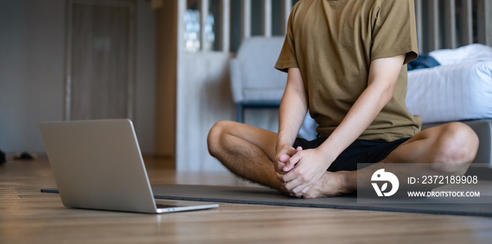 男人在家学习锻炼，早上用笔记本电脑在线学习瑜伽。锻炼