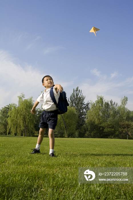在草地上玩纸飞机的小男孩