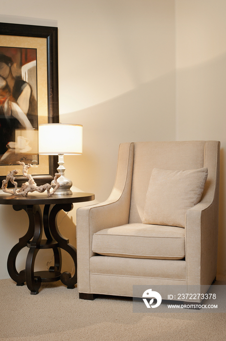 Armchair by lit lamp on console table against painting on wall at home; Scottsdale; USA