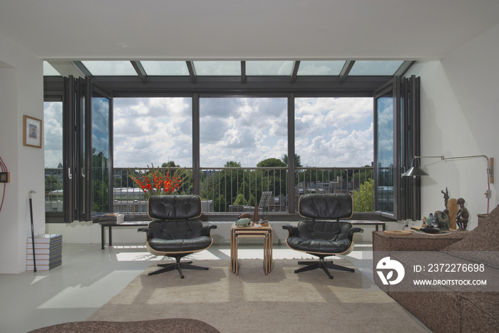 Leather armchairs in living room with view of trees and clouds through window