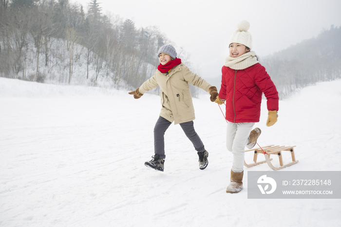 快乐的小孩在雪地上拉着雪橇奔跑
