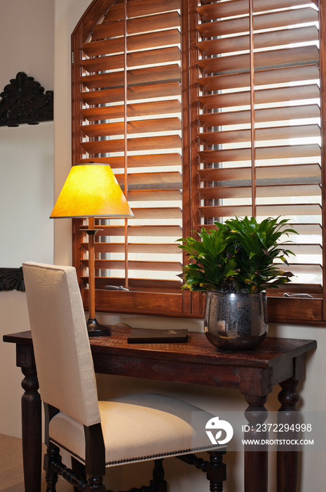 Close-up of a chair at console table with lit lamp and wooden blinds at home; Scottsdale; USA