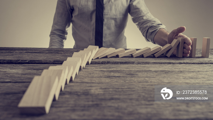 Businessman preventing dominoes from crumbling with palm