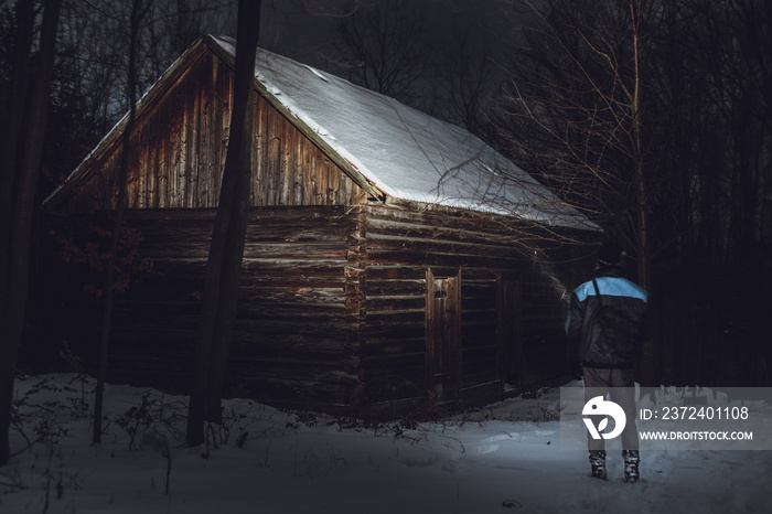 Man (photographer) standing in front of the abadoned and creepy cottage in forest in winter. Man on 