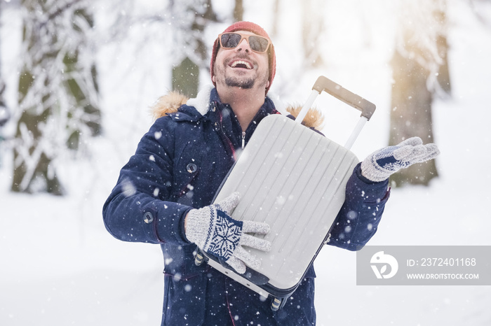 年轻时尚男子在雪地上拿着行李箱竖起大拇指的肖像。寒假tr