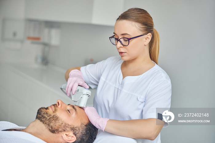 Charming female esthetician treating male skin with laser device