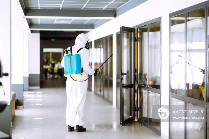 Disinfecting of office to prevent COVID-19, Man in protective hazmat suit with  with spray chemicals