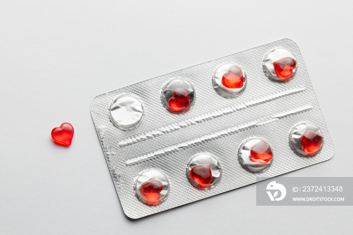 Love pills. Blister pack with red heart shaped pills. Tablets for lovers or potency. Gray background