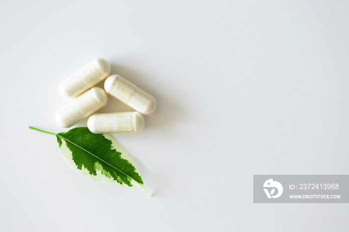 Pill capsules heap and plant leaf on white background with copy space, top view. Concept alternative