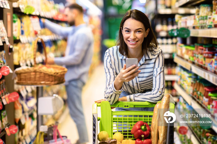 Young woman with mobile phone shopping in hypermarket