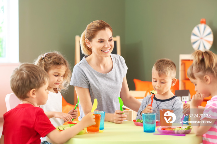 Nursery teacher with cute little children during lunch in kindergarten