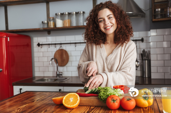 健康的高加索女性在家用新鲜蔬菜烹饪沙拉时微笑的照片