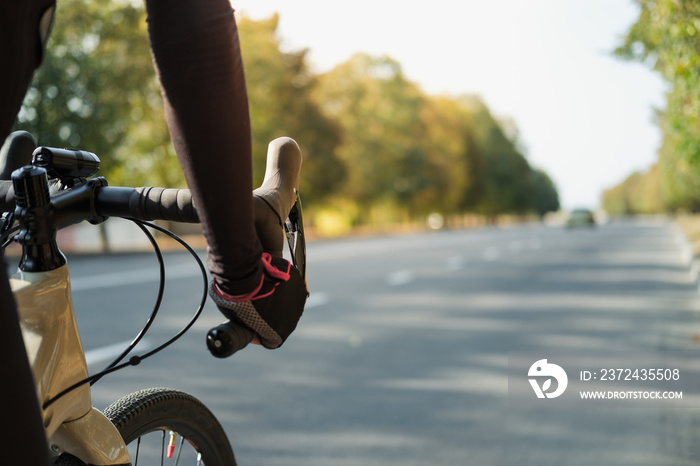 Hands of a cyclist resting on road bike handlebars, road view with copy space. Cycling, bicycle spor